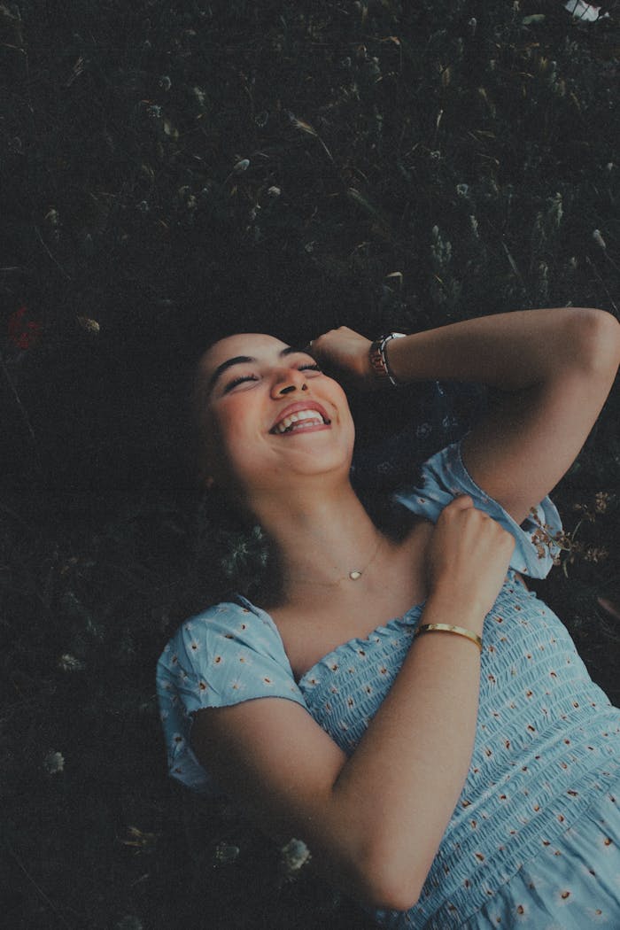 Smiling woman in a blue dress lying on grass, enjoying a peaceful moment in Morocco.