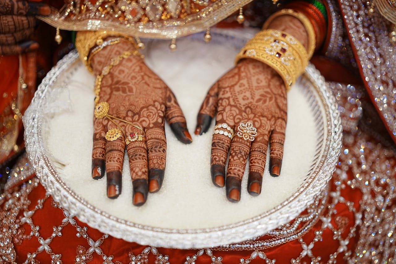 Intricate bridal henna on hands adorned with gold jewelry, captured in vibrant detail.